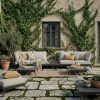Modulare Gartenlounge Kombination aus zwei 2-Sitzer Modulen aus anthrazitfarbenem Aluminium mit integriertem Tisch und Beistelltisch vor Landhauswand
